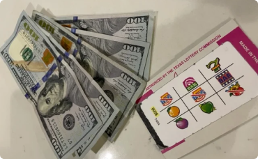 A winning lottery ticket with symbols and several $100 bills fanned out next to it.