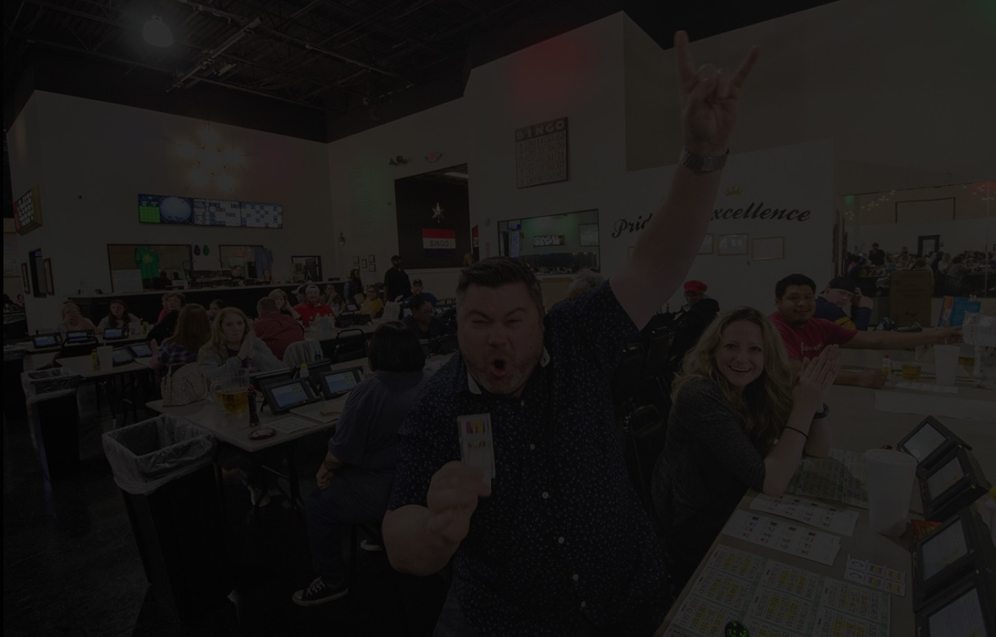 A group of people at a bingo hall, smiling with bingo cards and devices on the table.
