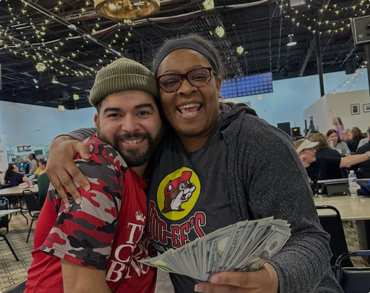 A group of people at a bingo hall, smiling with bingo cards and devices on the table.